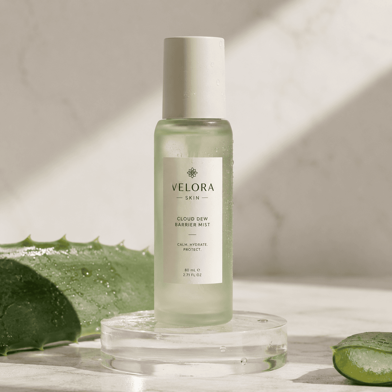 Velora Skin Cloud Dew Barrier Mist bottle on an acrylic riser with aloe vera, still-life product photo
