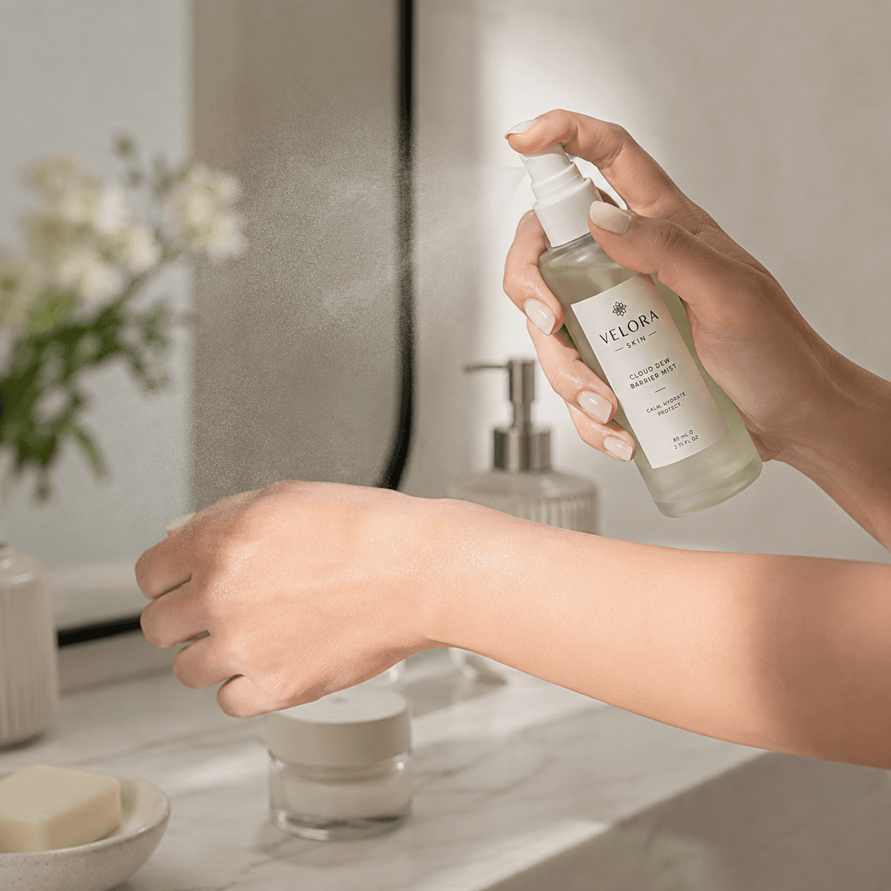 Hand spraying Velora Skin Cloud Dew Barrier Mist onto the wrist in a bright bathroom, in-use product photo